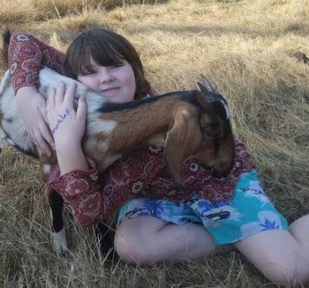 10-year-old girl in the grass hugging a goat.